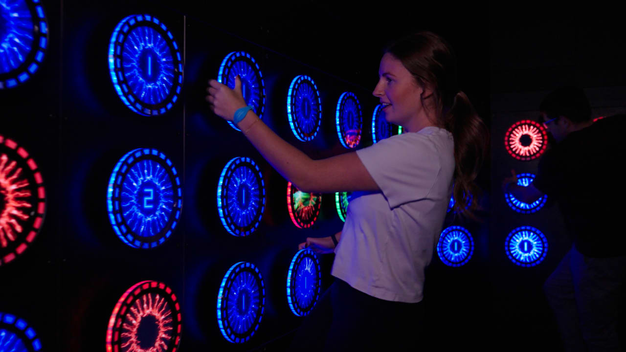A player presses illuminated circular targets in the Grip room.