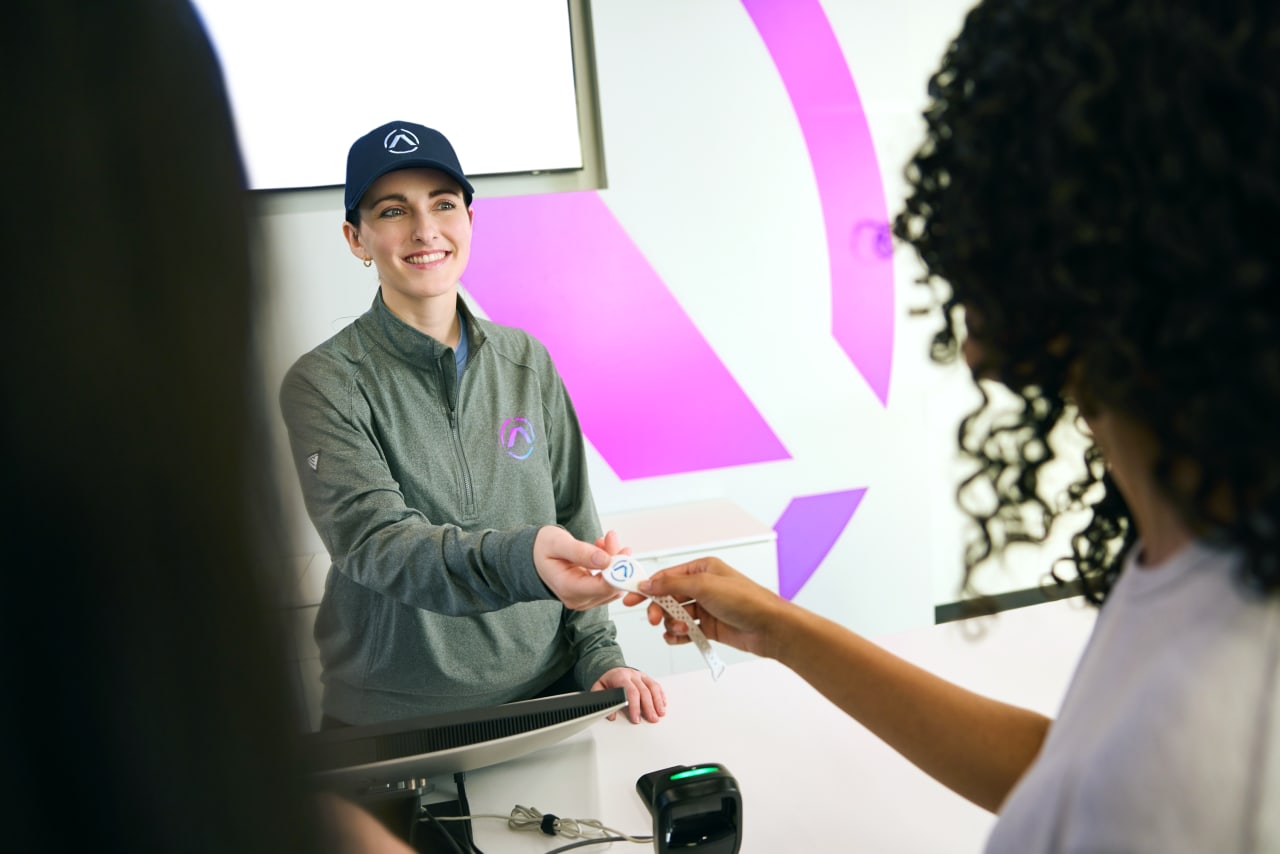 A smiling Activate staff member hands a wristband across the counter.