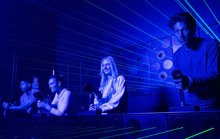 Players compete at a lit rail in a room washed in blue light.
