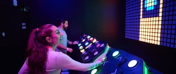 Two players working a glowing control panel in an Activate game room.