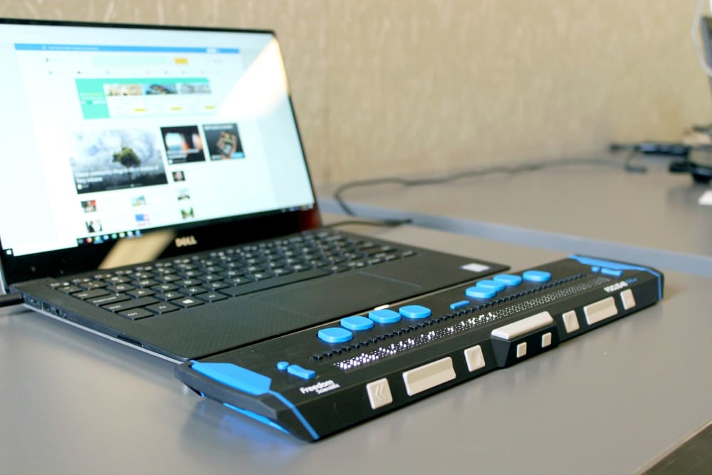 A dell laptop computer browsing a website, with a refreshable braille display attached