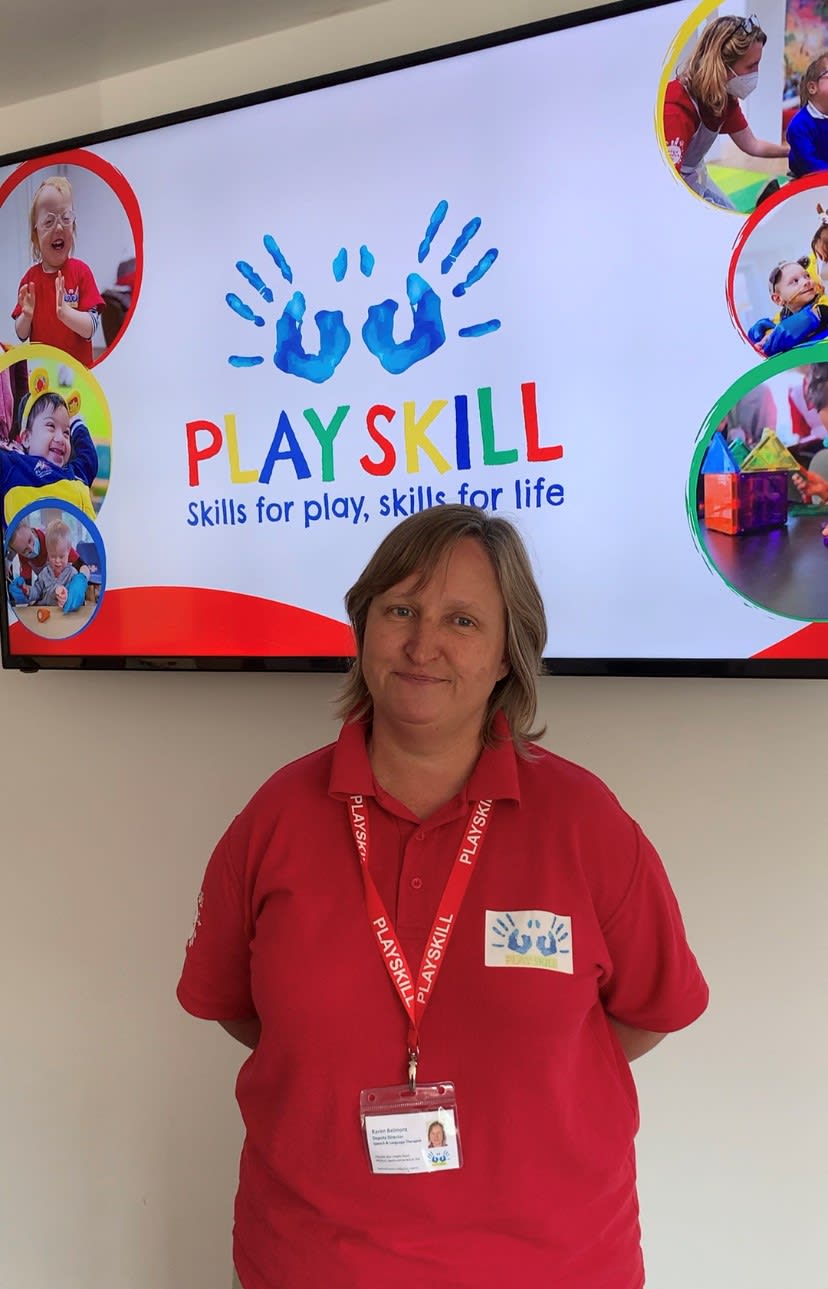 A Playskill team member smiling at the camera. A display in the background shows the playskill logo.