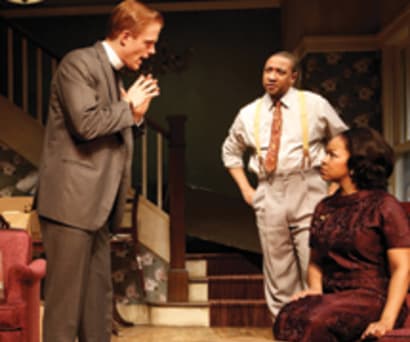 Actors Christina Kirk, Jeremy Shamos, Annie Parisse, Brendan Griffin, Damon Gupton, and Crystal A. Dickinson in Clybourne Park. Everyone is in a living room with moving boxes scattered about. Griffin stands as he talks to Dickinson, who is seated.