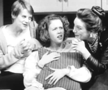 Black and white photo of actors Kellie Overbey, Julie Lund, Kristine Nielsen, and Nat DeWolf in Betty's Summer Vacation. Overbey, Lund, and De Wolf sit on the couch in pajamas. Nielsen leans over the back of the couch onto Lund's shoulder.