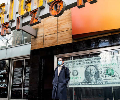 Artist Jilly Ballistic (wearing a navy blue trench coat, glasses, and black boots) stands in front of her piece outside Playwrights. It's a large dollar bill with a handwritten speech bubble reading, "Imagine 352,464 of these. Now imagine they're bodies."