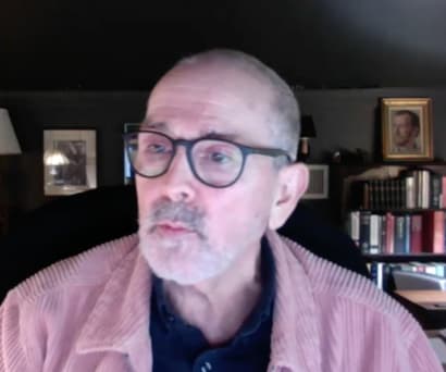 Playwright Craig Lucas, a white male wearing glasses and a pink corduroy shirt open over a black shirt, leads a virtual Master Class.
