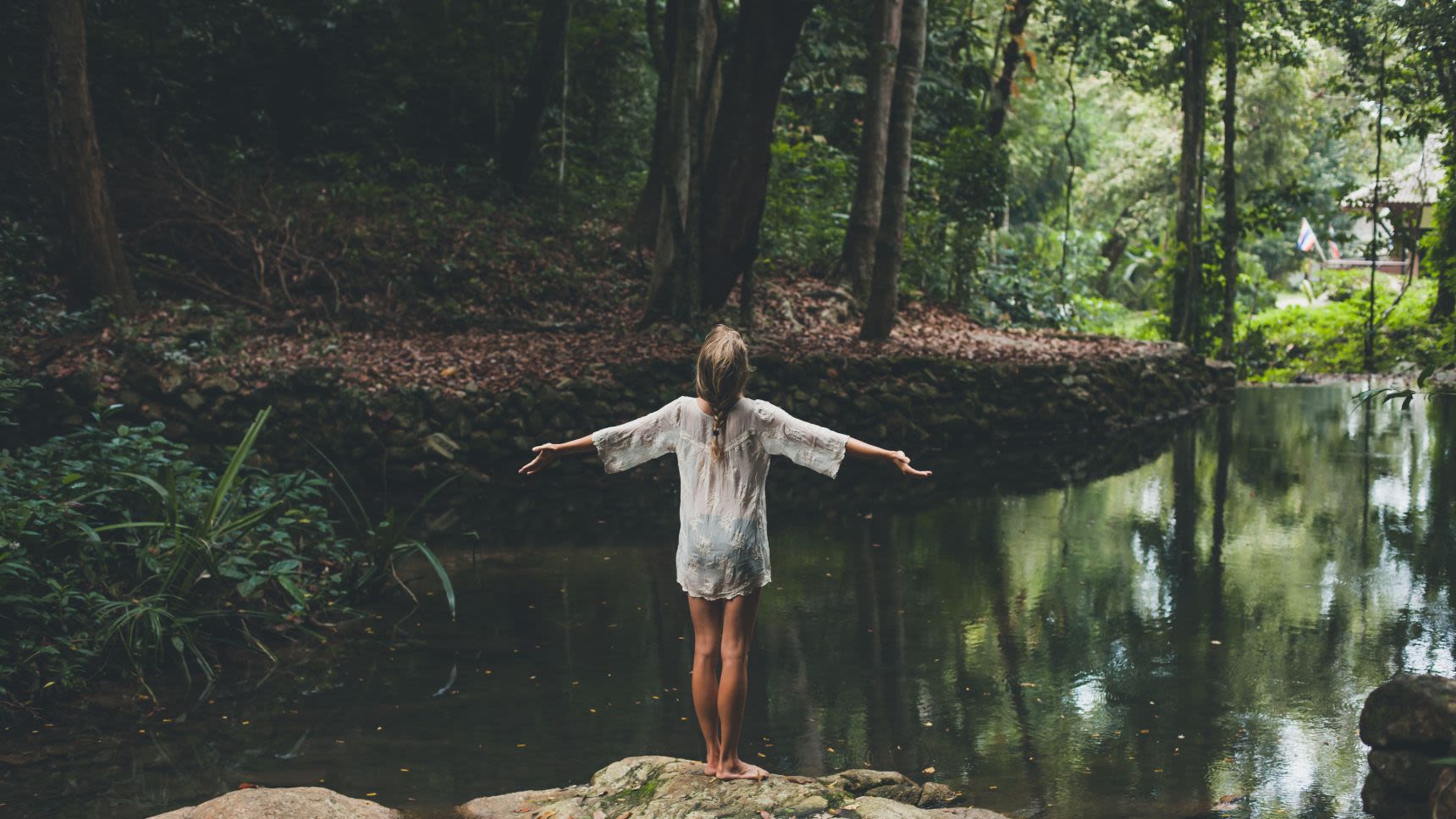 woman basking in nature while standing at edge of creek