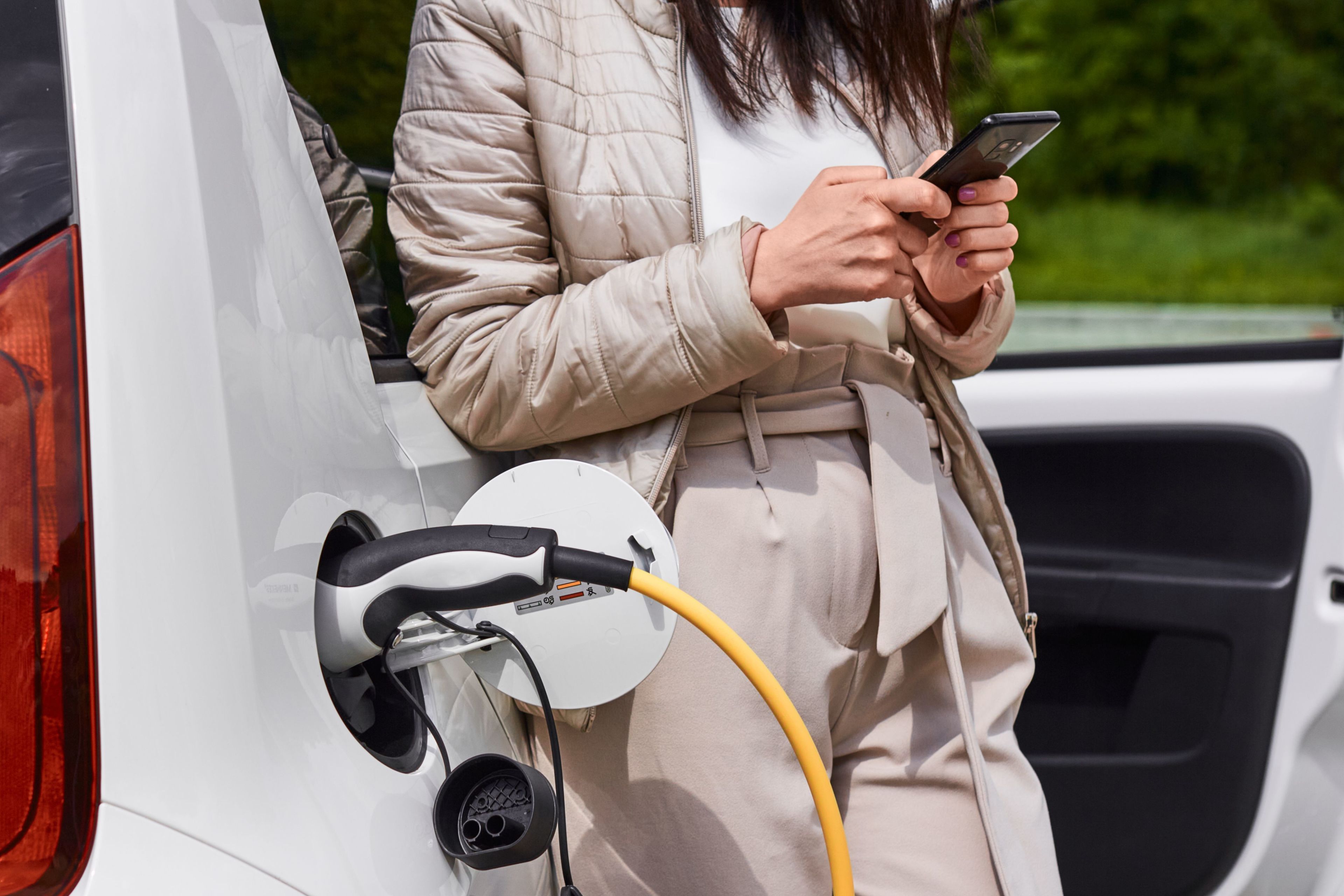 woman stands by electric vehicle as it charges