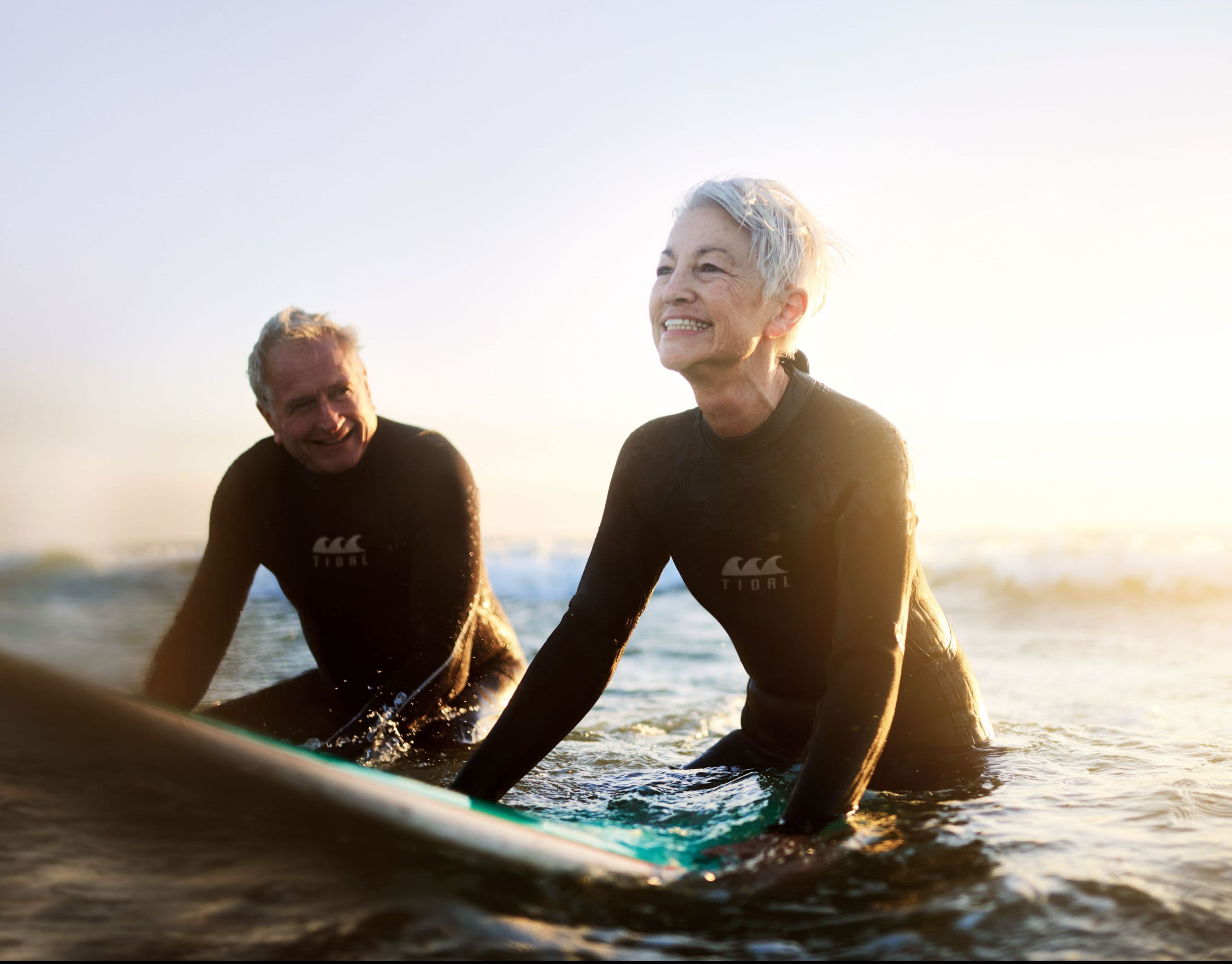 An older couple with grey hair surfing in the ocean