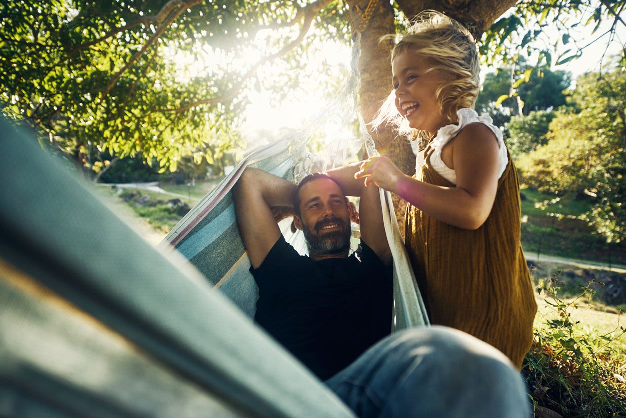 Smiling father and daughter in sunny yard while dad swings on the hammock