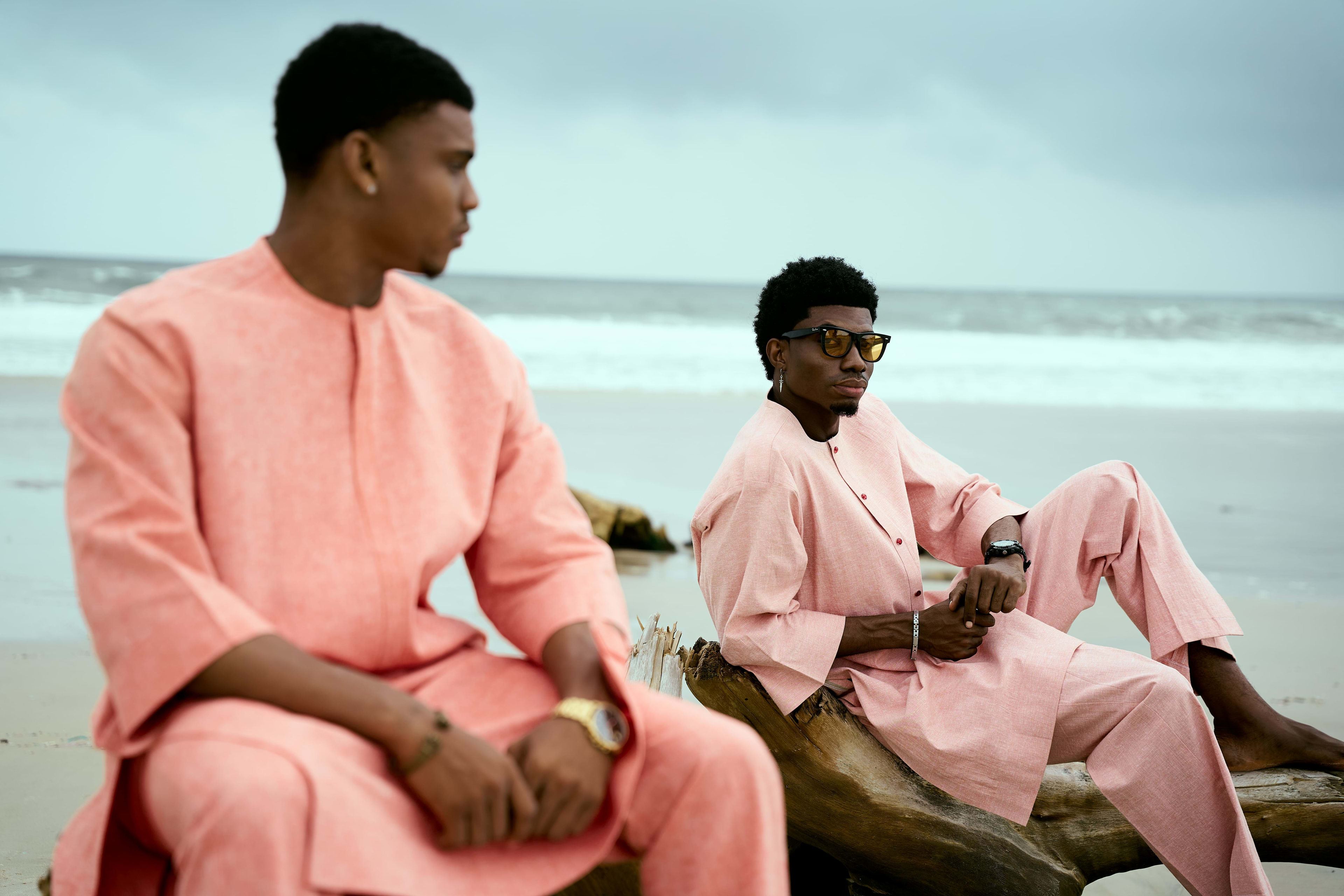 Two OnPoint models in matching coral two-piece sets, seated on driftwood at the beach