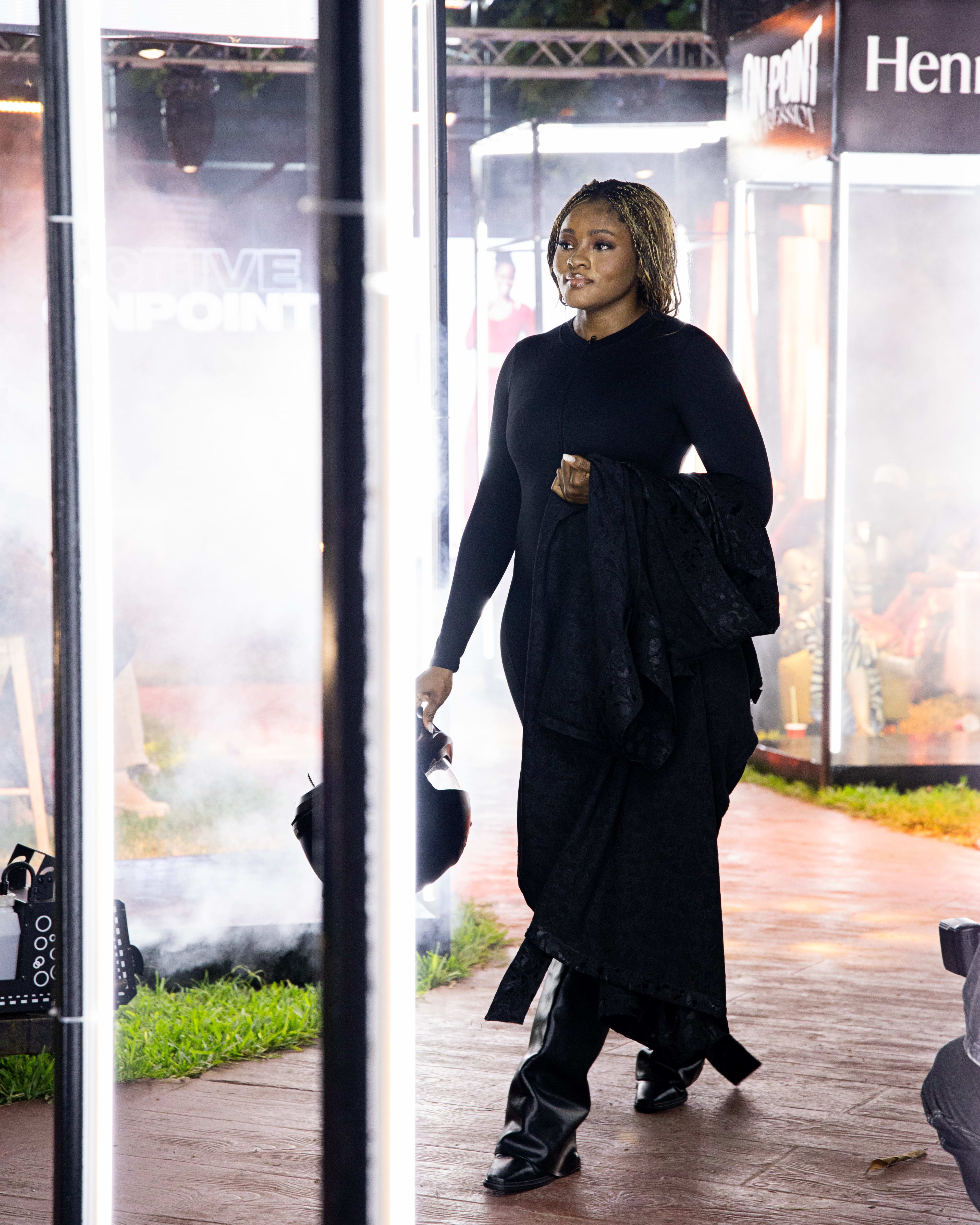 A model in a black draped, sheer-layered look walking through a fog-lit doorway