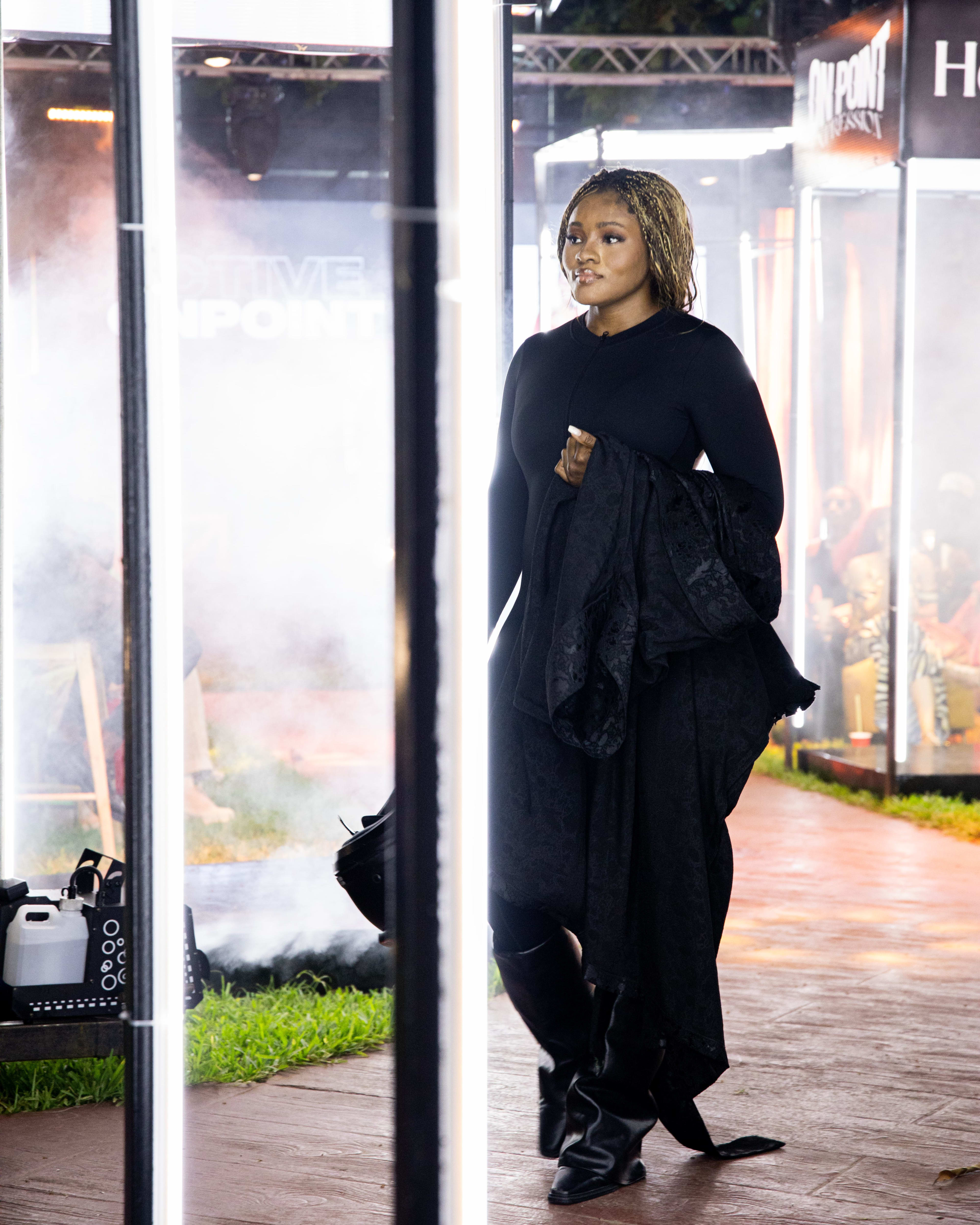 A model in a black top and dark maxi skirt walking off the runway into stage fog, jacket in hand