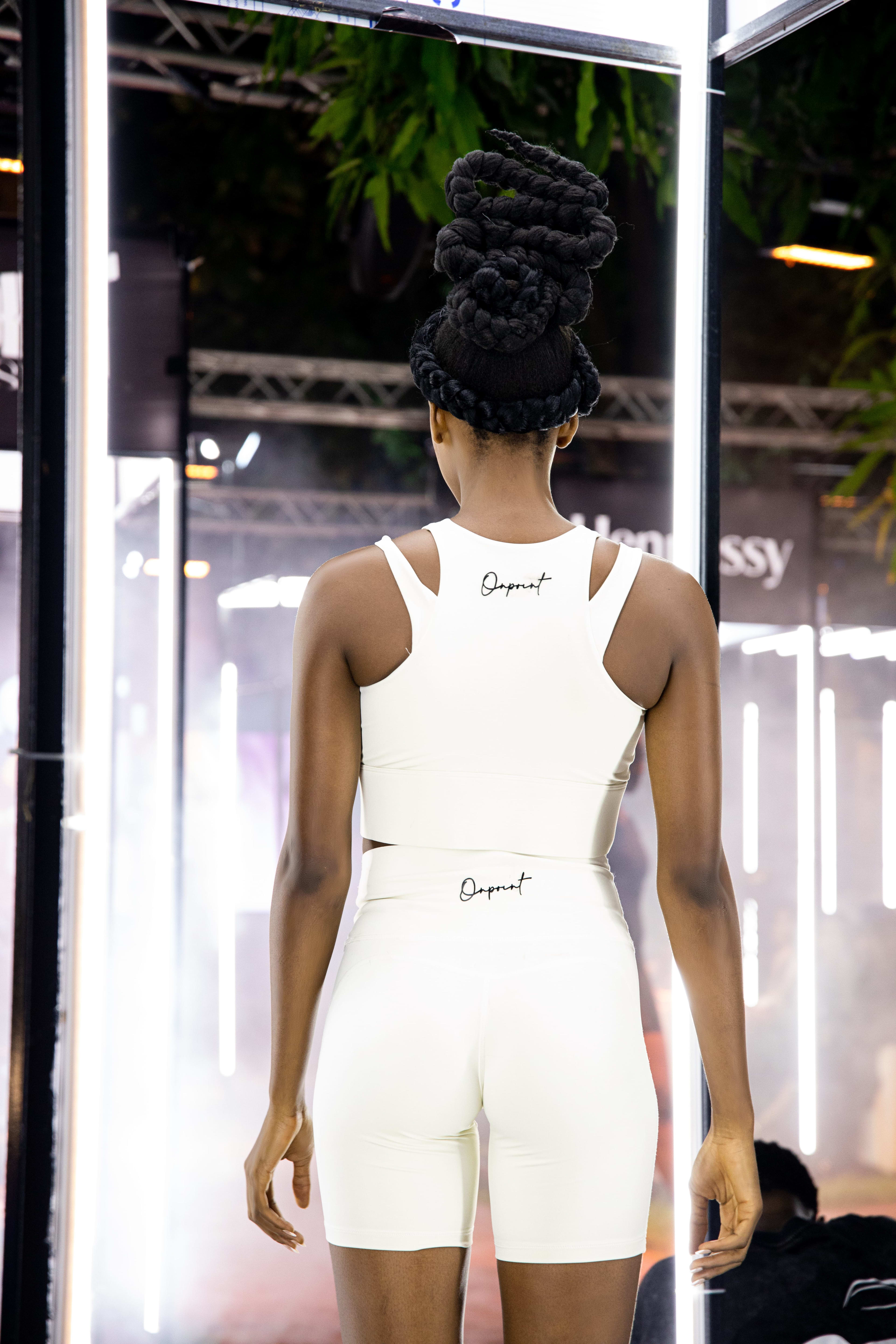 A model's back view in white Onpoint-branded activewear crop top and biker shorts, hair in braided buns