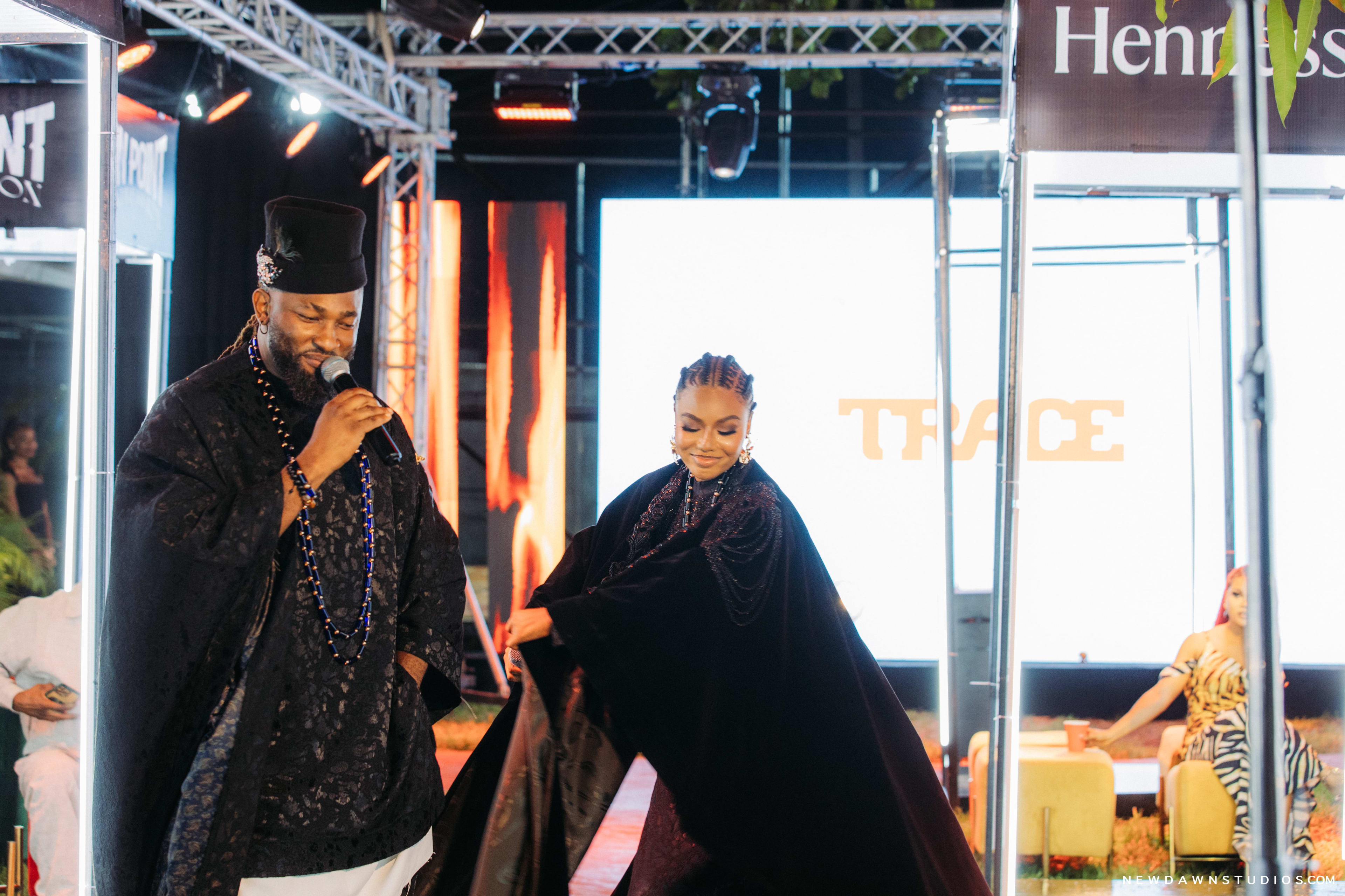 The hosts walking the runway, the female host's cape caught mid-motion