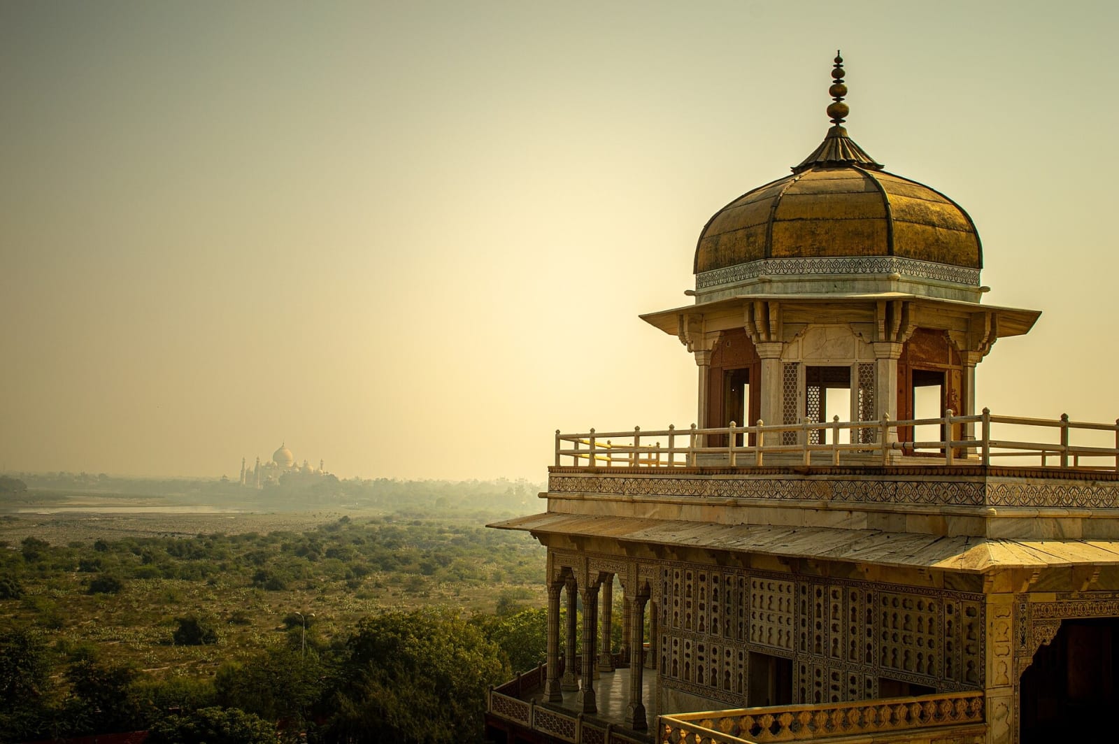 The Musamman Burj tower at Agra Fort at dusk with the Taj Mahal faint in the haze