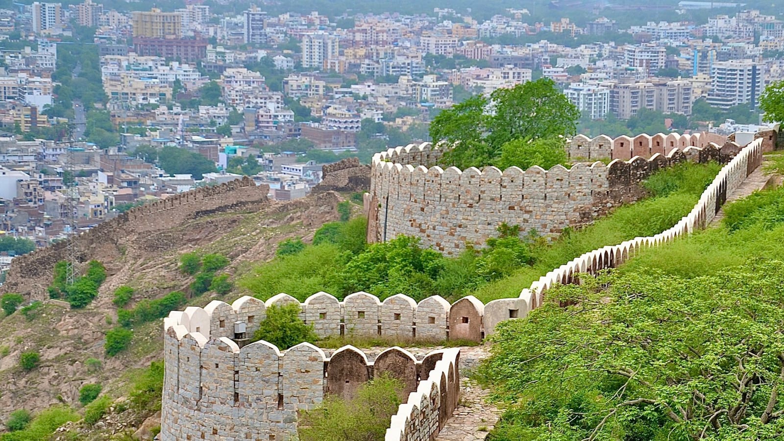 Crenellated wall of Nahargarh Fort running down a green hillside above the houses of Jaipur