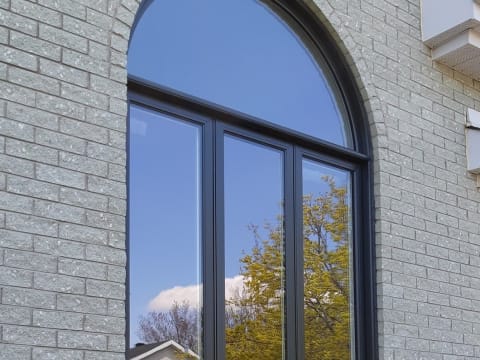 Grande fenêtre arquée noire sur une façade de brique
