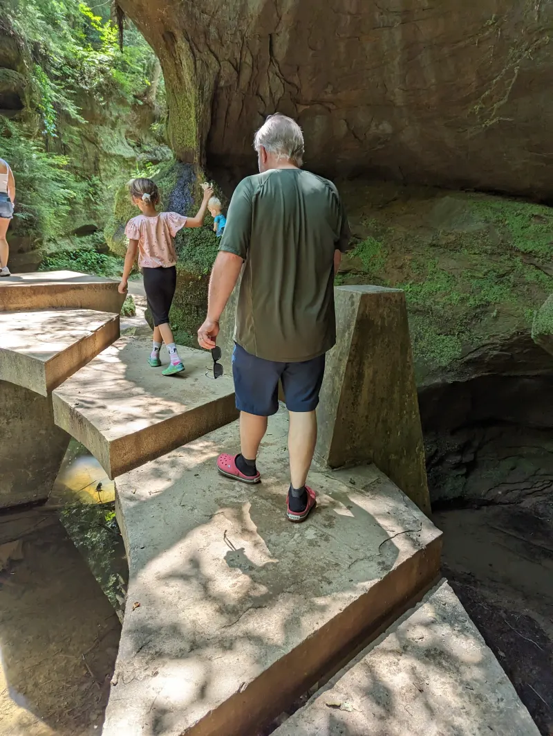 An adult and child on stone steps beside a rock wall at Old Man’s Cave.