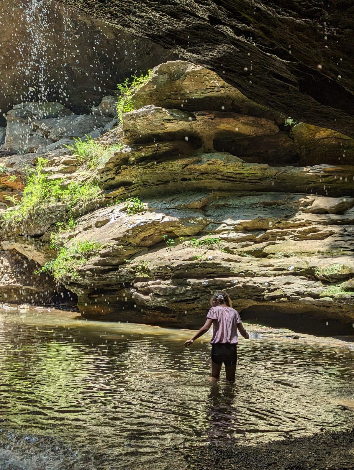 Child wading through the gorge pool at Old Man's Cave in June, Hocking Hills Ohio, with waterfall mist falling from sandstone ledges above