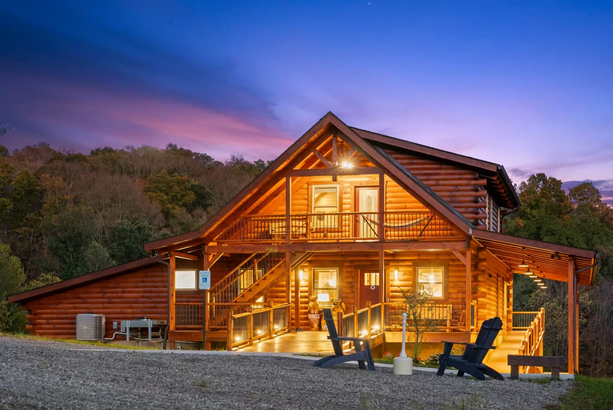 Pool House Lodge cabin exterior at dusk with fall foliage — wide angle view of multigenerational cabin in Hocking Hills Ohio — vaulted log ceiling, stone fireplace, and sectional seating for 20 guests in Hocking Hills Ohio