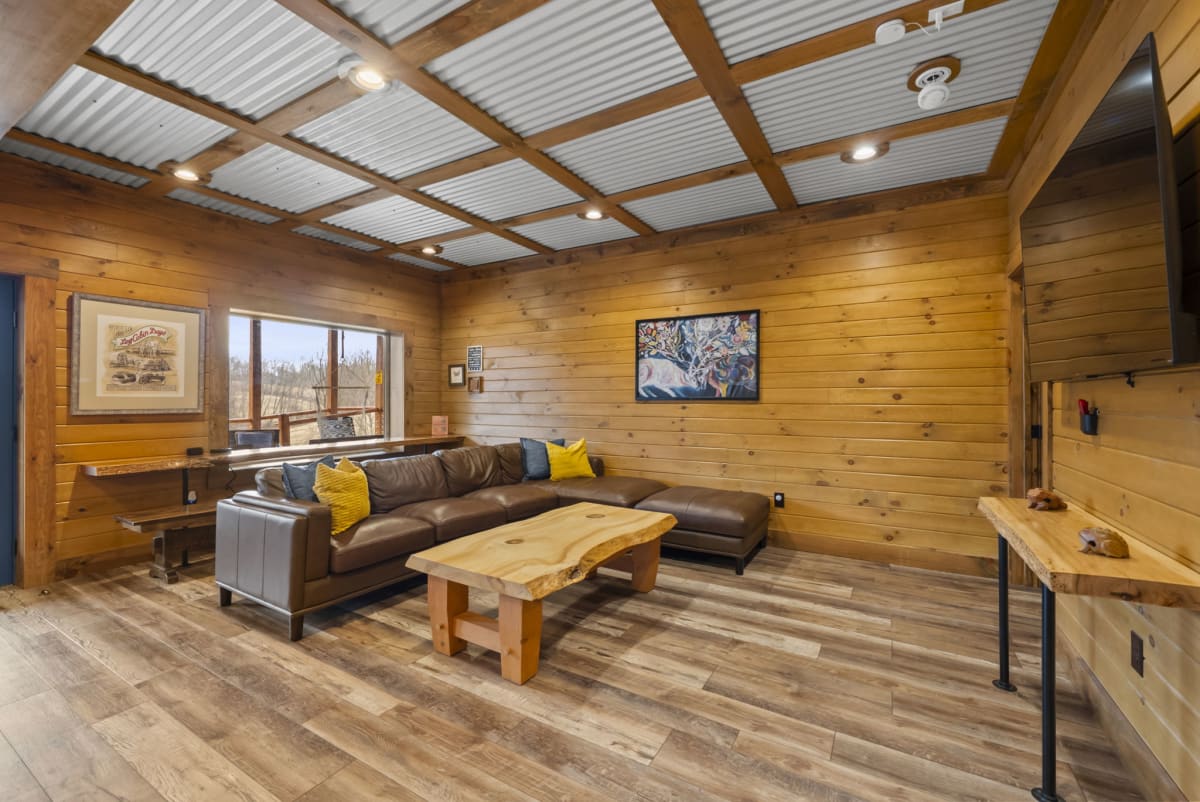 Lower level TV lounge at Pool House Lodge — leather sectional, live-edge coffee table, Hocking Hills Ohio cabin
