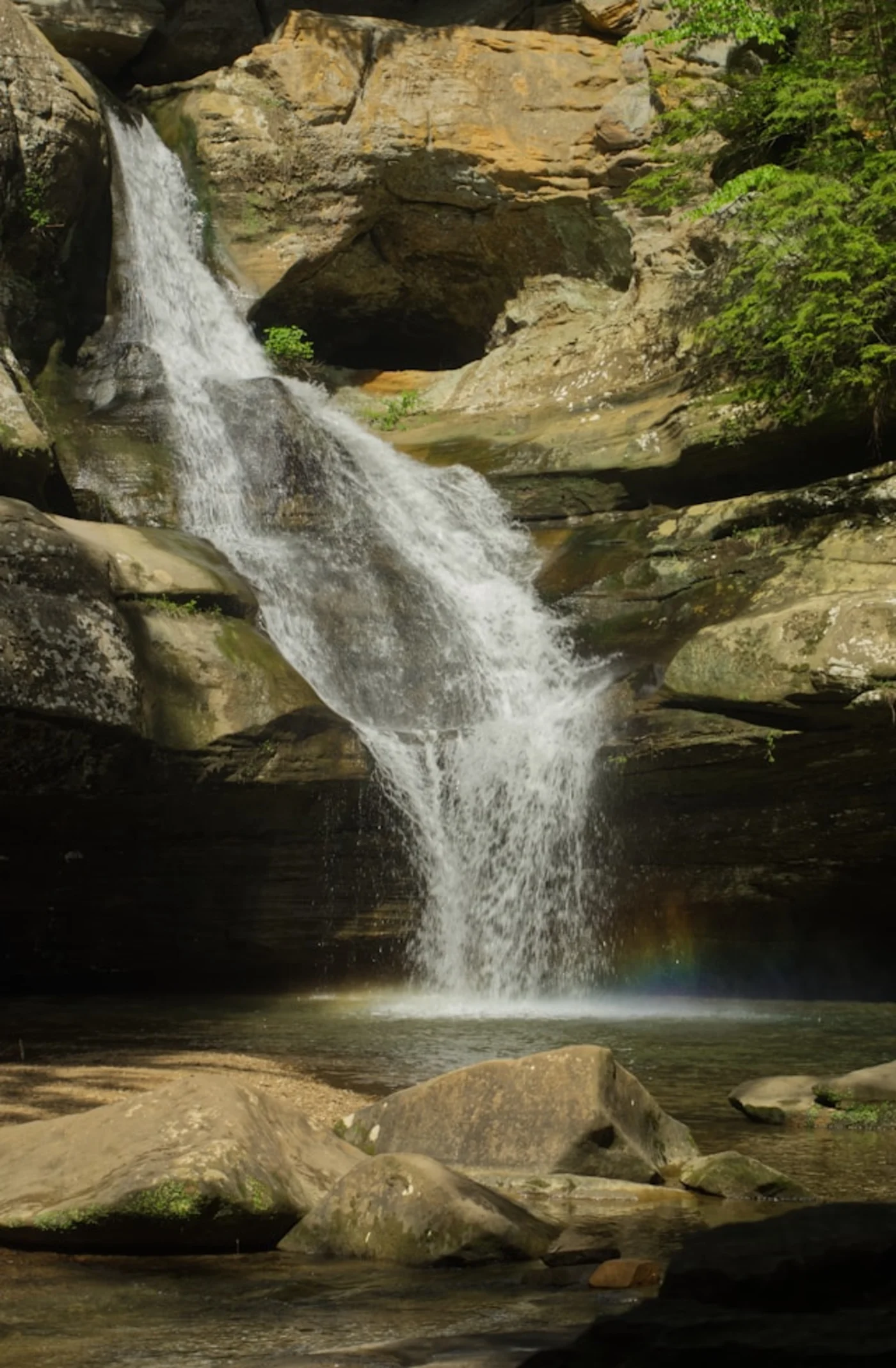 A high-flow waterfall over sandstone cliffs with fresh spring foliage, Hocking Hills in April