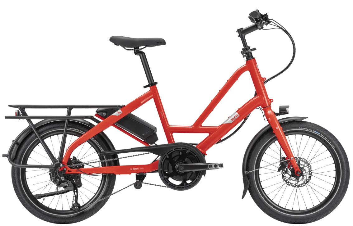 A bright red electric bicycle with a black frame, fenders, racks, and wheels, against a black background.