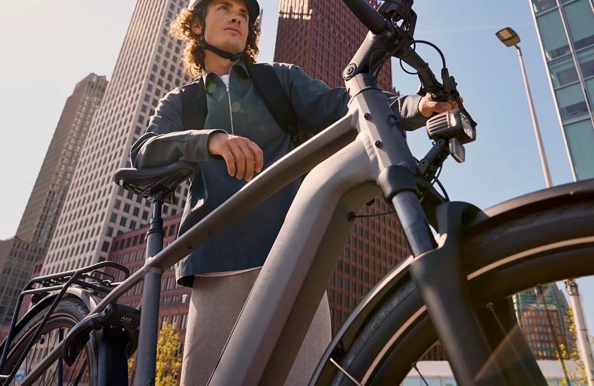 Man with curly blond hair wearing a helmet and a green jacket on an electric bicycle.