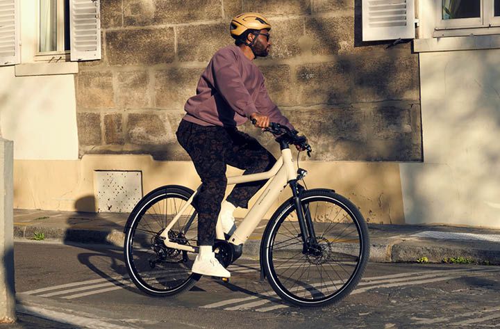 A man wearing a purple sweater and yellow helmet rides a white electric bike.