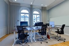 Banérgatan 16 - Större kontorsrum med ljusgrå väggar och ljusinsläpp från två stora fönster. Inspirationsbild från liknande lokal.