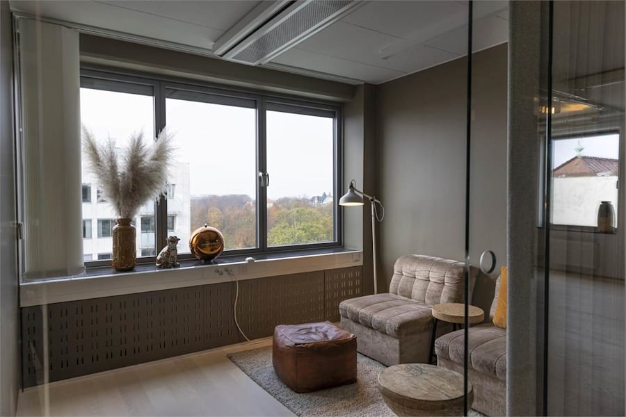 Södra Tullgatan 3 - Sittgrupp i glasat samtalsrum med utsikt över grönska.