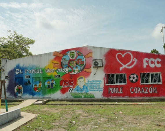 Colorful mural on a building wall featuring a soccer ball, community scenes, and the text "El fútbol nos une" and "Ponle corazón."