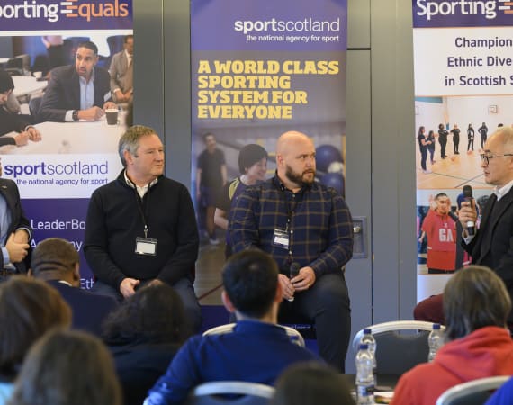 Two men sitting and talking at an event.