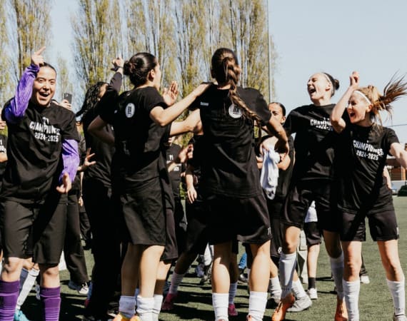 A group of female soccer players celebrate together on a field, wearing matching Champions 2022-2023 shirts.