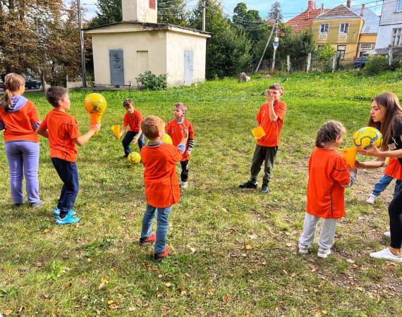 Children play soccer on a red outdoor court, wearing bright green and red bibs.