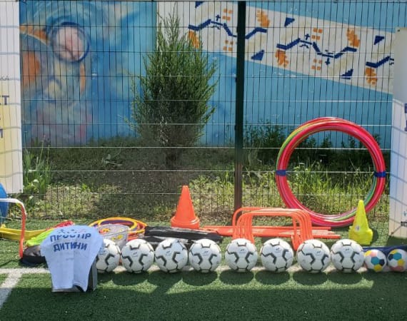 Assorted sports equipment, including soccer balls and cones, arranged on a grassy field near a colorful mural.