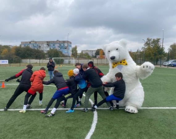 A group of children playfully participate in tug-of-war with a person in a large white bear costume on a soccer field.