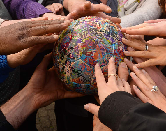 A group of diverse hands touch a colorful, graffiti-covered ball, symbolizing unity and cooperation.