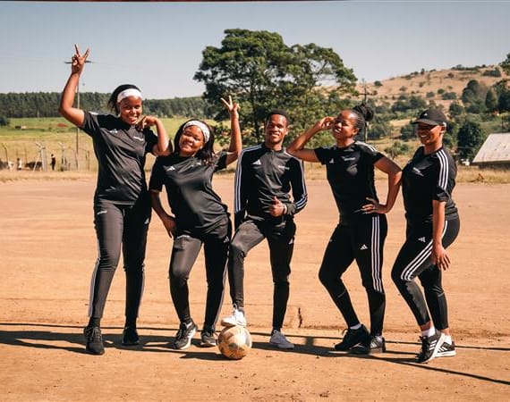 Four women in adidas soccer uniforms smiling together for a team photo.