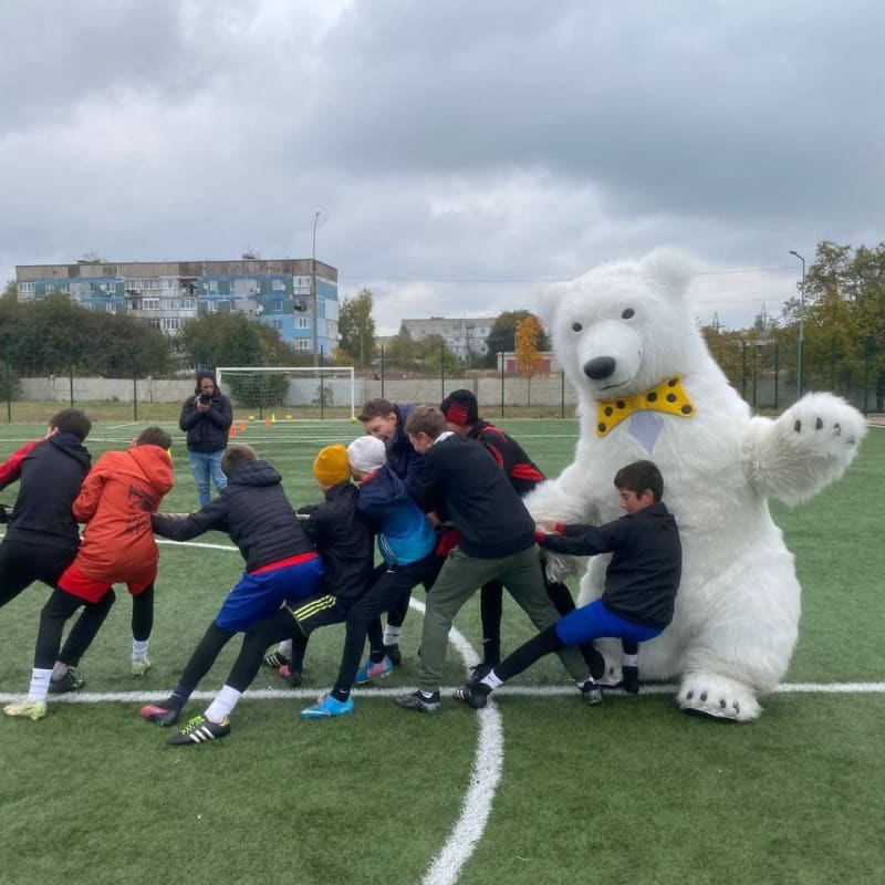 A group of children playfully participate in tug-of-war with a person in a large white bear costume on a soccer field.