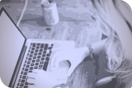 Una mujer usa su laptop en una mesa, mientras su bebida se encuentra en el mismo lugar.