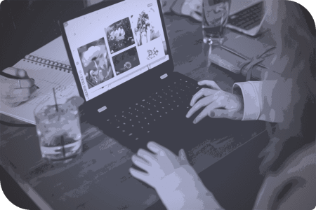 Una mujer usa un laptop en una mesa, mientras bebe un bebido.