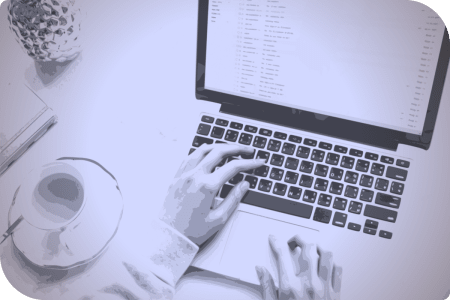 Una persona está trabajando en su computadora, con una taza de café a su lado.