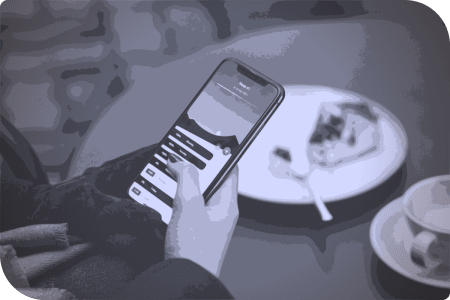 Una persona está usando su celular mientras está sentada en una mesa con un plato de pastel.