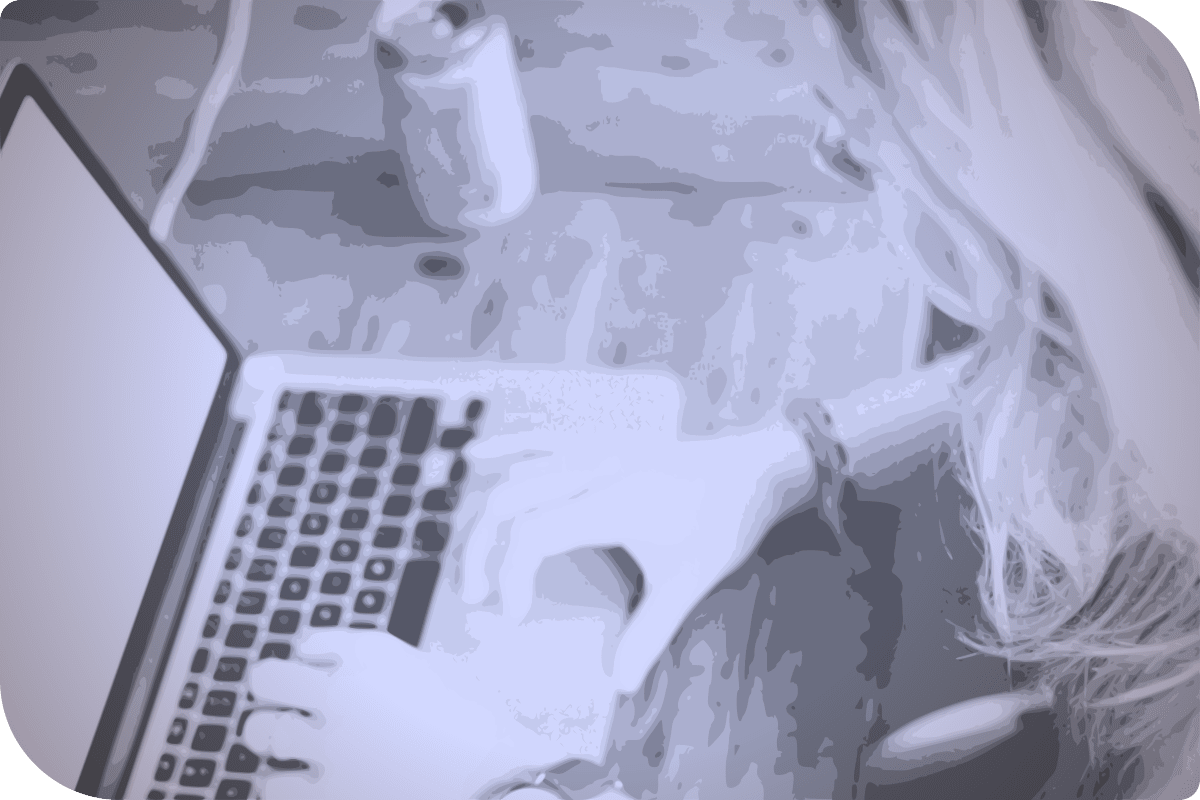 Una mujer usa su laptop en una mesa, mientras su bebida se encuentra en el mismo lugar.