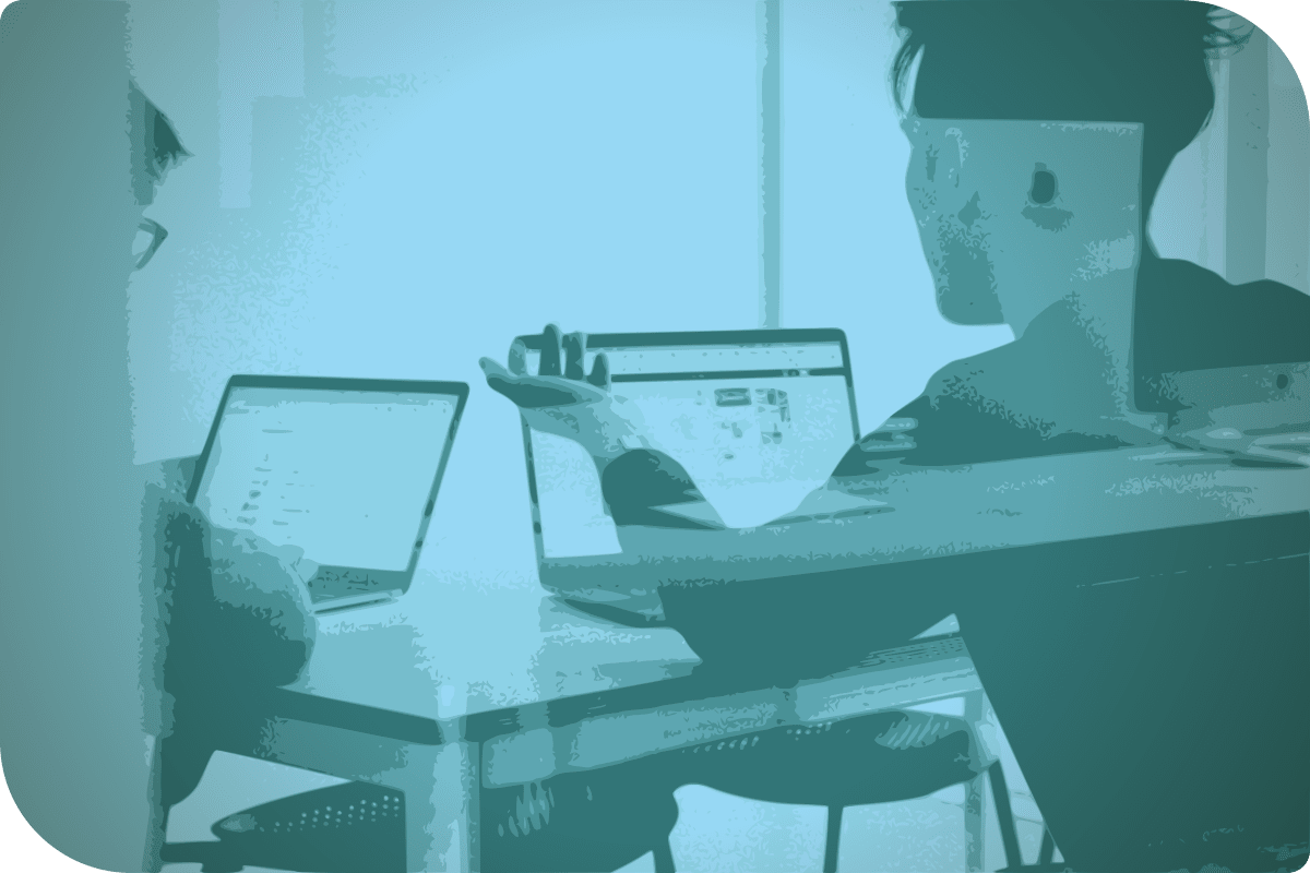 Dos personas están sentadas en una mesa, cada una con su propia computadora.