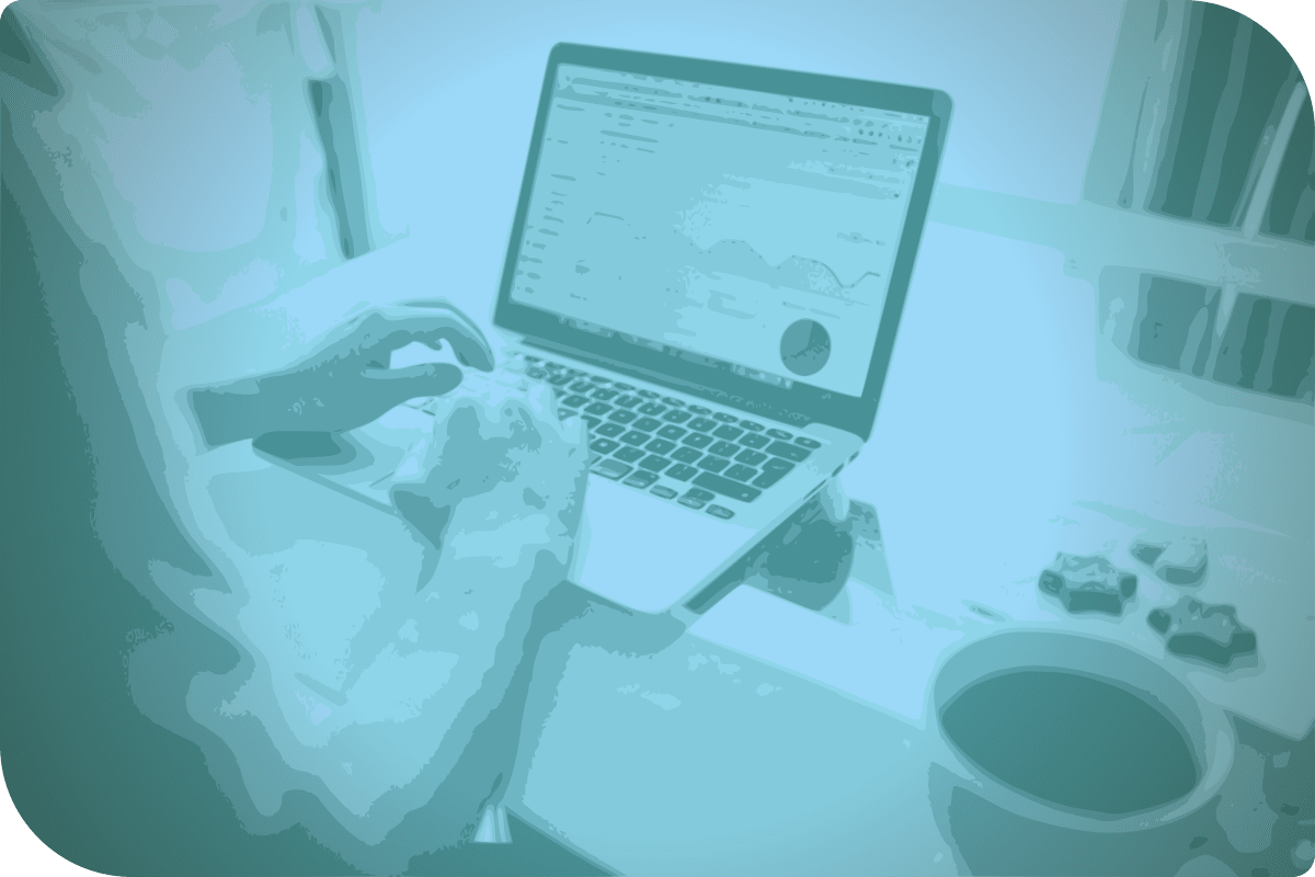 Una persona está trabajando en su computadora, que está en una mesa con un café y un plato de chocolates.
