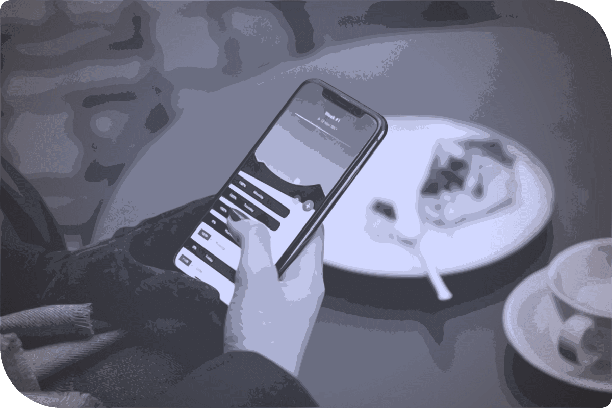 Una persona está usando su celular mientras está sentada en una mesa con un plato de pastel.