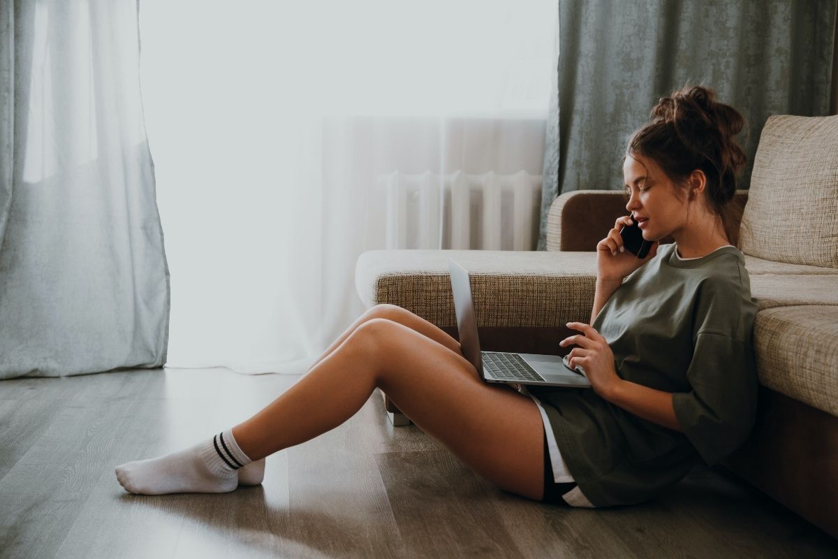 Mujer sentada con su computador y hablando por teléfono. 